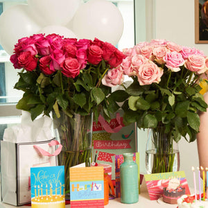 hot pink & bicolor pink roses in a glass vase on a table with celebration material